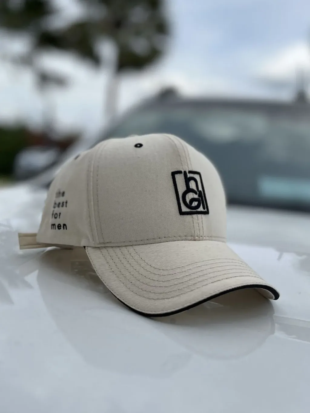 Boné dad hat bege personalizado com logo bordado sobre o capô de um carro. Modelo aba curva discreto da Fênix Personalizados.
