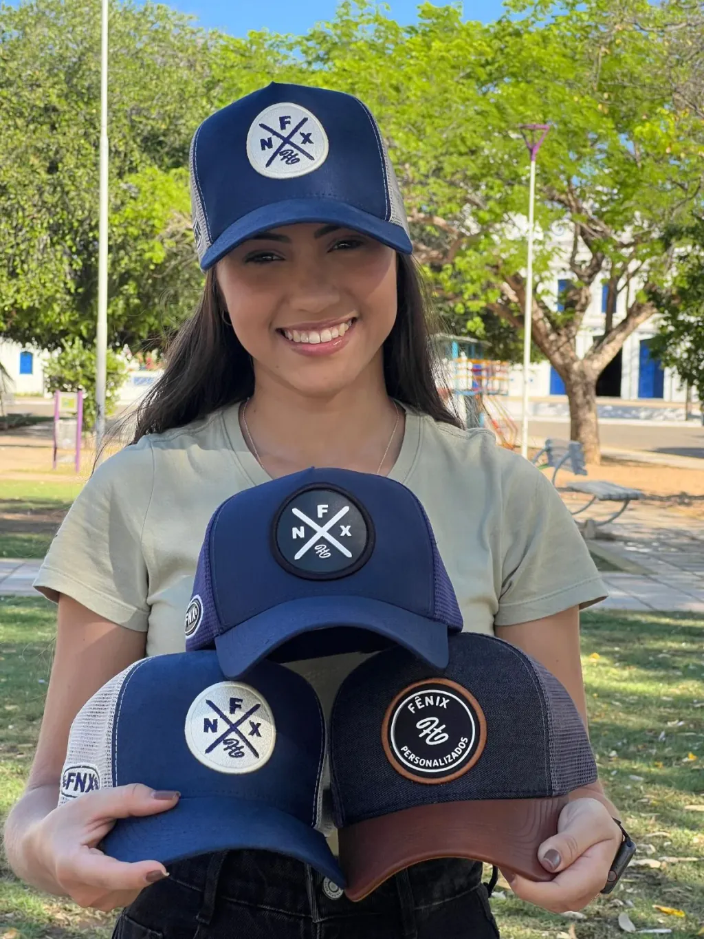 Jovem segurando três bonés trucker azul-marinho personalizados com patch emborrachado. Produção em atacado da Fênix Personalizados.