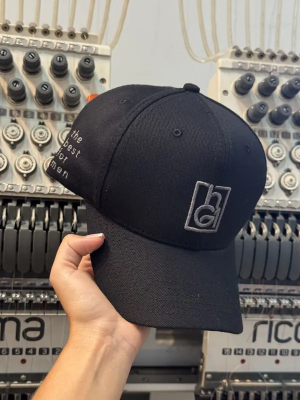 Boné personalizado preto sendo bordado em máquina industrial. Bordado de alta qualidade feito na fábrica da Fênix Personalizados.