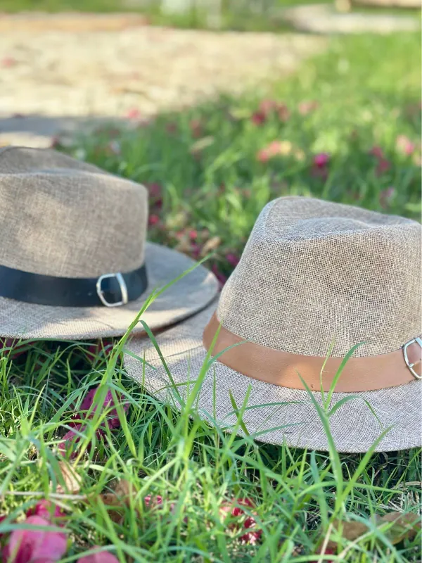 Chapéus de palha personalizados com faixa de couro e fivela sobre a grama. Modelos de aba larga produzidos pela Fênix Personalizados.